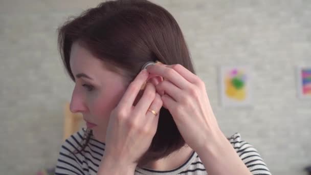 Young woman inserts a hearing aid into her ear — Stock Video