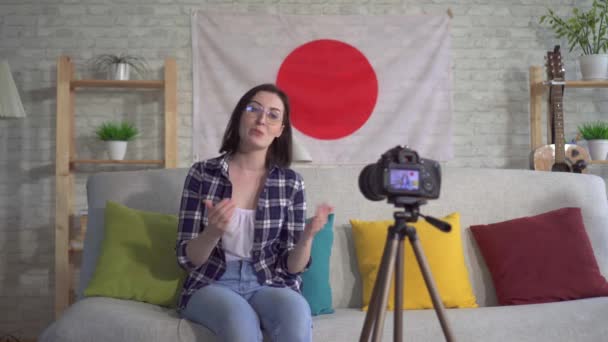 Jovem blogueiro mulher na camisa no fundo da bandeira do Japão grava um vídeo — Vídeo de Stock