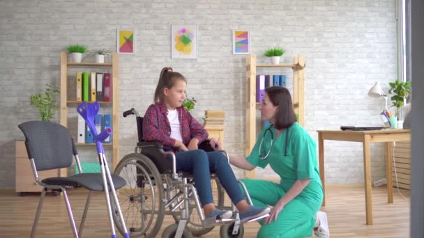 Médecin examine la jambe d'une adolescente handicapée dans un fauteuil roulant — Video