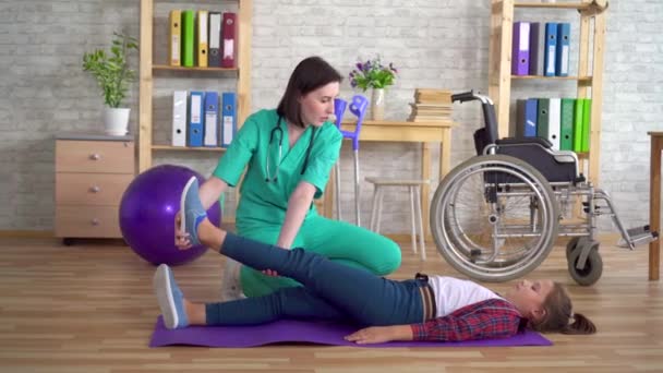 Physiotherapist in the rehabilitation center helps in warming up the legs of a teenage girl in rehabilitation after a spinal injury — Stock Video