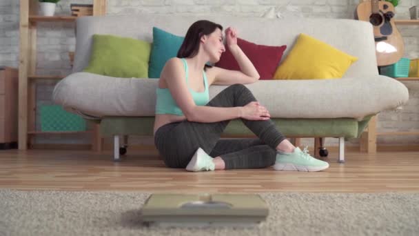Szomorú, csalódott fiatal sportos nő sír a padlón nézi a mérleg — Stock videók