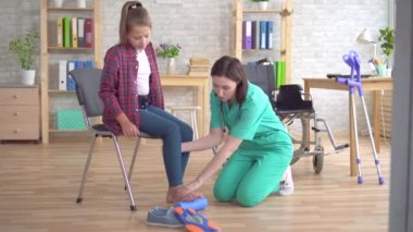 Doktor bir tekerlekli sandalyede bir genç kızın bir silindir yardımıyla bacak germek için rehabilitasyonda yardımcı olur