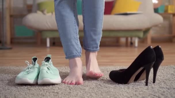 Женщина выбирает туфли на высоких каблуках вместо кроссовок — стоковое видео