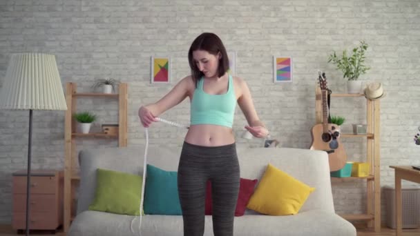 Выражающая радость молодая женщина в спортивной одежде использует измерительную ленту — стоковое видео