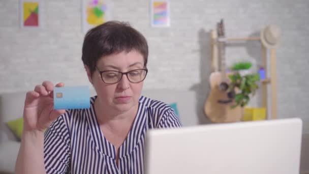 Frustrerad kvinna sitter på en bärbar dator med ett bankkort i handen — Stockvideo