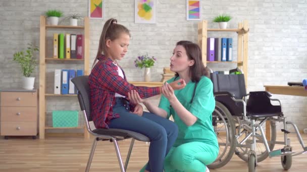 Doktor bir yaralanma dan sonra tekerlekli sandalyede bir genç kızın elini inceler — Stok video