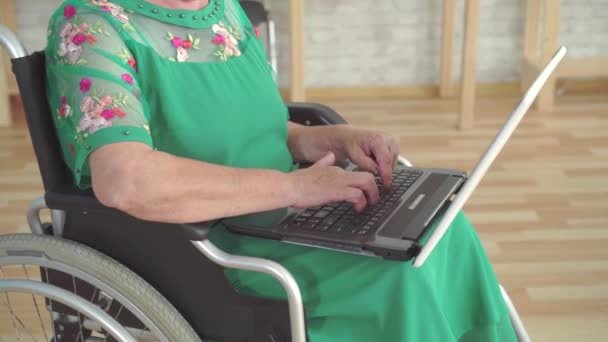 Крупним планом літня жінка вручну друкує на ноутбуці і сидить у інвалідному кріслі — стокове відео