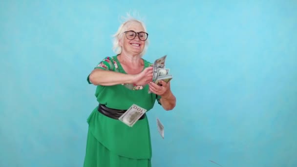 喜びに満ちた肯定的な高齢女性は、青い背景に紙幣を投げるスローモーション — ストック動画