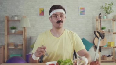 Masada oturan sebze yiyen bıyıklı mutlu ve neşeli genç sportif adam