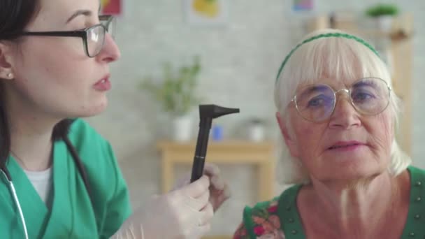耳鼻咽喉科医は耳鏡をクローズアップして老婦人の耳を調べる — ストック動画