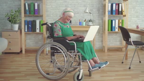 車椅子で障害のある幸せな笑顔の高齢女性は、ラップトップを使用しています — ストック動画
