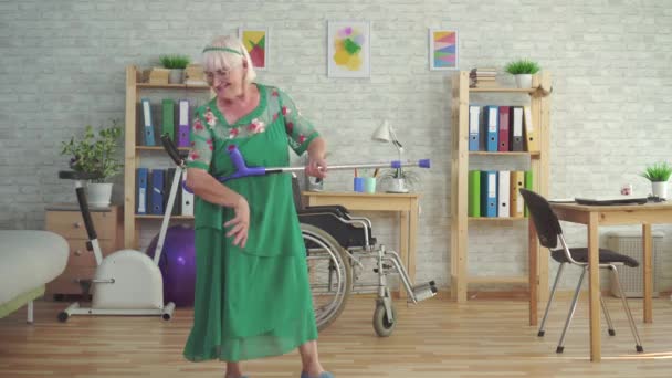 Cheerful expressive elderly woman dances with crutches and plays like a guitar — Stock Video