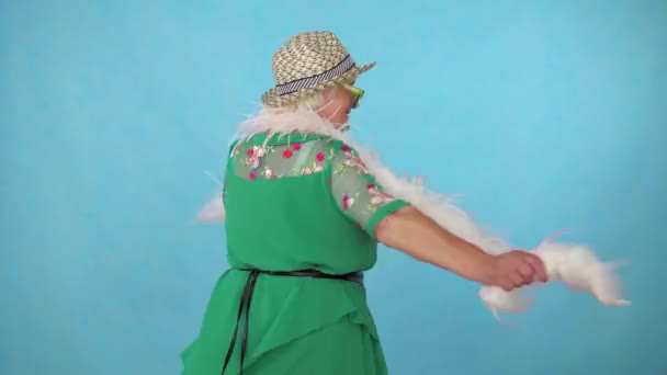 Alegre expresiva enérgica anciana en un sombrero y boa bailando sobre un fondo azul — Vídeo de stock