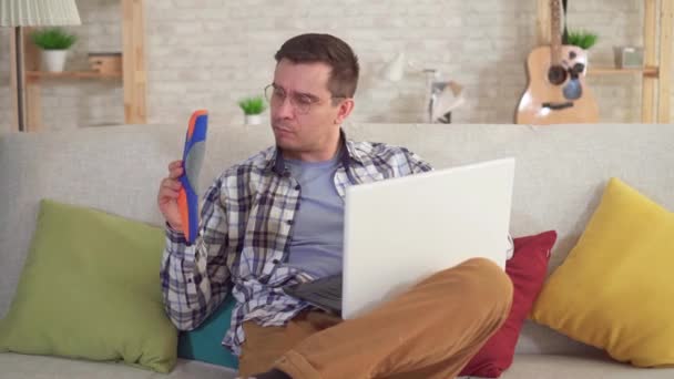 Hombre sentado en una mesa utiliza un ordenador portátil y sostiene plantillas ortopédicas en la mano — Vídeo de stock