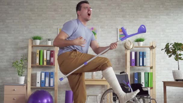 Expressieve man met een verbonden been dansen met krukken in het revalidatiecentrum slow mo — Stockvideo