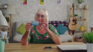 Gri saçlı düşünceli yaşlı kadın banka kartı tutar