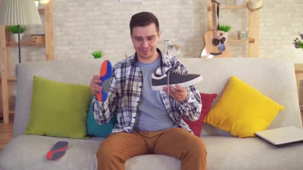 Человек, сидящий на диване вставляет ортопедические стельки в обувь — стоковое видео
