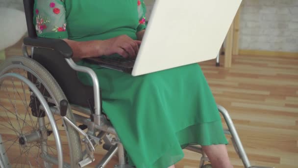 Glad leende äldre kvinna funktionshindrade i en rullstol använder en bärbar dator närbild — Stockvideo