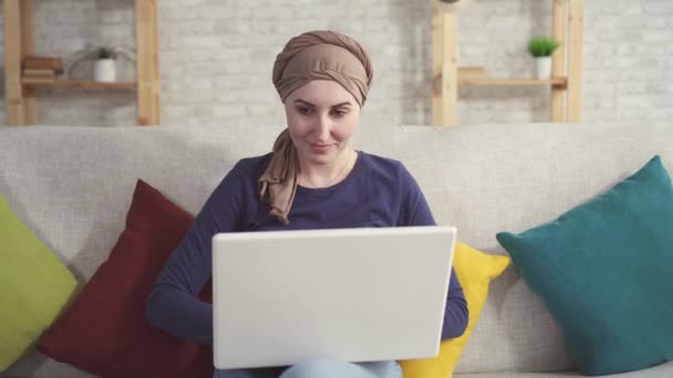 Portret jonge vrouw met kanker in een sjaal na chemotherapie met een laptop — Stockvideo
