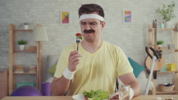 Hombre infeliz con sobrepeso y bigote con un tazón de ensalada sobre la mesa. El concepto de pérdida de peso — Vídeos de Stock