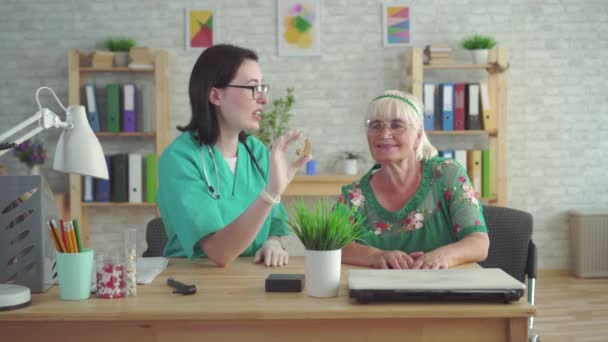Klinikte doktor yaşlı kadının kulağına bir işitme cihazı koymak için yardımcı olur — Stok video