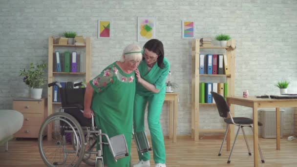 Infermiera aiuta una donna anziana a scendere da una sedia a rotelle — Video Stock