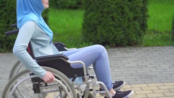 Positive junge behinderte Frau im muslimischen Hidschab-Kinderwagen bei einem Spaziergang im Park — Stockvideo