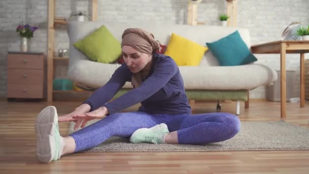 Ung kvinna cancerpatient efter kemoterapi i en halsduk på huvudet gör stretching innan träningen hemma — Stockvideo