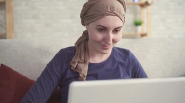 kemoterapi sonrası kafasına bir eşarp kanser olan pozitif genç kadın bir dizüstü bilgisayar kullanır