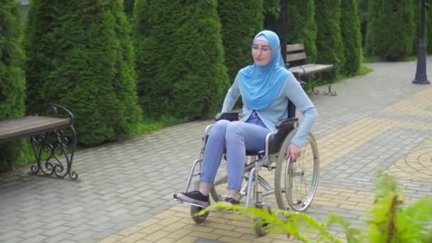 Молодая арабская женщина-инвалид в очках и традиционном шарфе в инвалидном кресле — стоковое видео