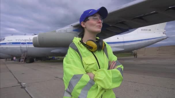 彼の手を横切ってポーズをとる航空機の背景に肖像画の女性空港労働者が近くに微笑む — ストック動画