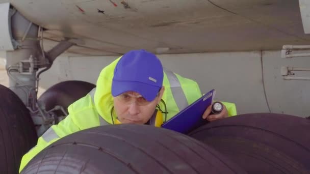 Специалист-специалист проводит техническую проверку шасси пассажирского самолета в аэропорту — стоковое видео