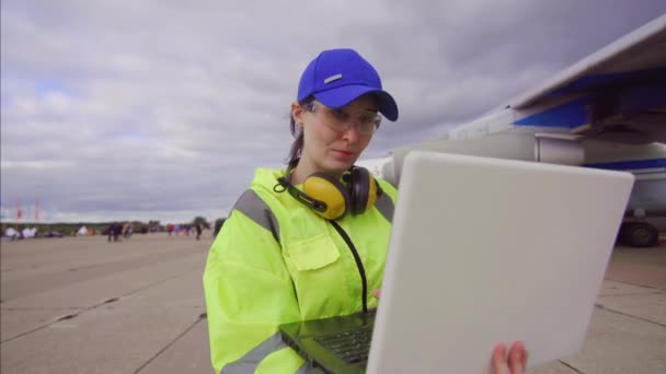 Mujer especialista con el ordenador portátil en uniforme en el aeropuerto en el fondo de un avión de pasajeros — Vídeos de Stock