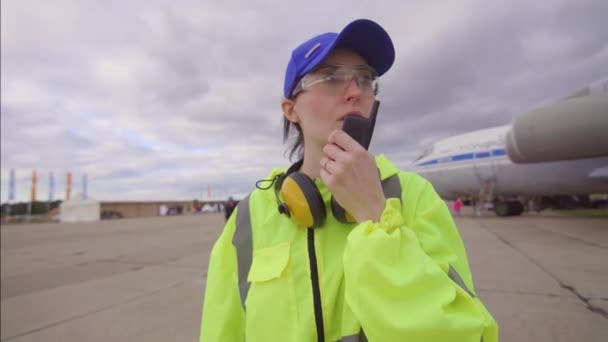 Flughafenarbeiterin im Hintergrund des Flugzeugs, das im Radio spricht — Stockvideo