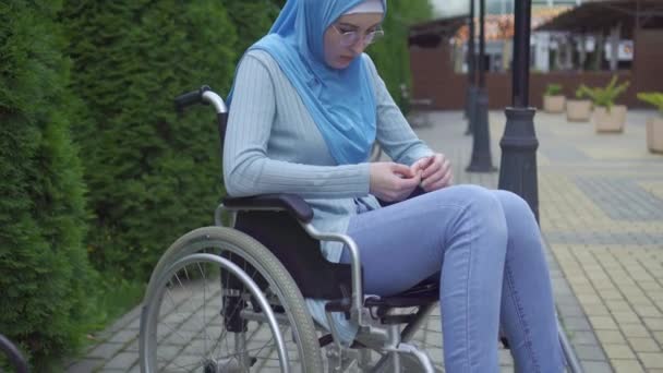 Portrét osamělé smutné mladé muslimské ženy v tradičním šátku sedícího na kolečkovém křesle v parku — Stock video