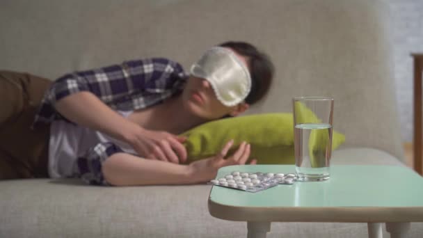 Jovem mulher em uma máscara de sono joga e vira em seu sono não pode dormir, em primeiro plano de pílulas de insônia — Vídeo de Stock