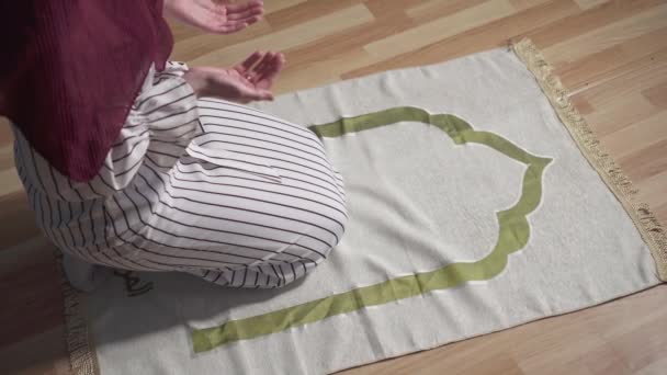 Мусульманська жінка в традиційному шарфі молиться на килимі у своїй вітальні вид зверху — стокове відео