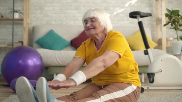 Aktiv positiv äldre pensionär engagerad i laddning och stretching på mattan i vardagsrummet närbild — Stockvideo