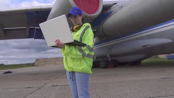 Specialista donna con computer portatile in uniforme in aeroporto sullo sfondo di un aereo passeggeri da vicino — Video Stock