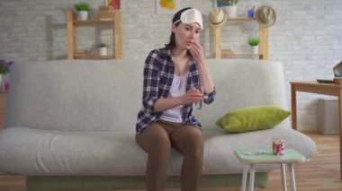Genç kadın uyku hapları alır ve uyku için bir maske kanepede uykuya gider