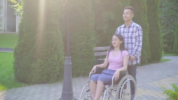 Jovem positivo asiático mulher deficiente em uma cadeira de rodas se comunica com seu amigo asiático — Vídeo de Stock