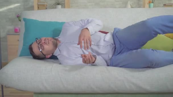 Az ember egy okostelefon volt epilepsziás roham otthon a kanapén közelről — Stock videók