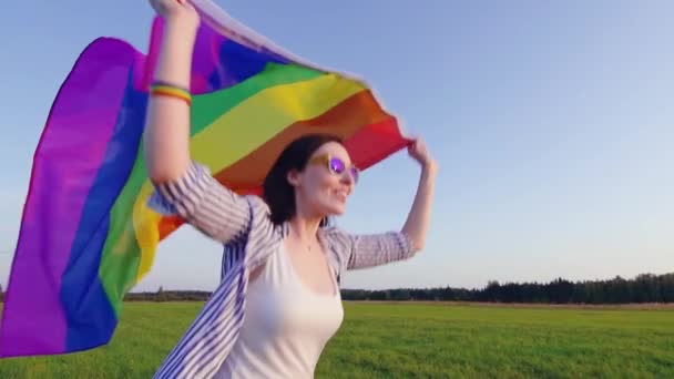 Joven atractiva mujer corre a través del campo con bandera LGBT lento mo primer plano — Vídeo de stock