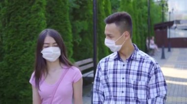 Yüzünde tıbbi maske olan iki genç Asyalı öğrenci sokakta yürürken ve yakından konuşuyor