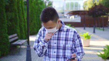 Yüzünde öksürük bir tıbbi maske ile genç Asyalı adam ve o bir akıllı telefon kullanır