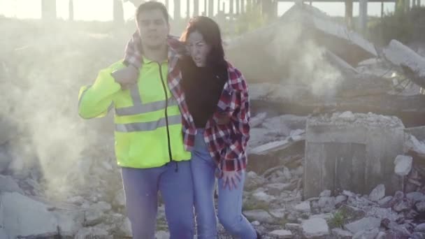 Male lifeguard in uniform assists a young woman on the ruins of a Smoking building — Stock Video