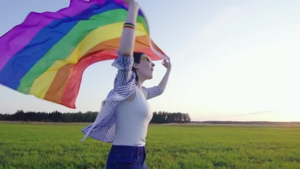 Jovem mulher atraente corre em campo com bandeira LGBT slow mo — Vídeo de Stock