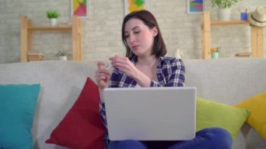 Dizüstü bilgisayar ile kanepede oturan gebelik testi ile genç çekici gülümseyen kadın