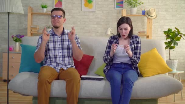 Jong getrouwd stel zittend in de woonkamer verheugt in een positieve zwangerschapstest — Stockvideo