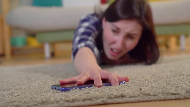 A young woman in a shirt had a heart attack and she tries to reach the smartphone lying on the floor slow mo — Stock Video